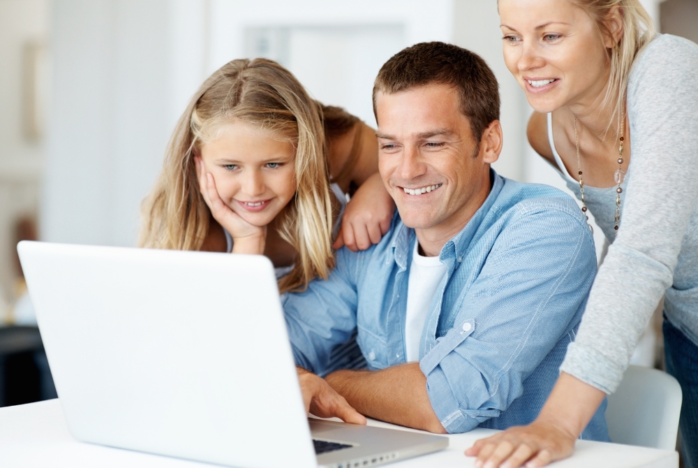 image of family gathered at the kitchen table looking at a laptop